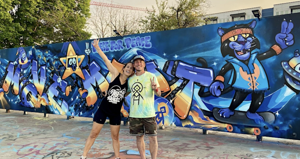 Artists pose in front of mural of cartoon panther riding a skateboard and making a peace sign at TOAH Outdoor Gallery