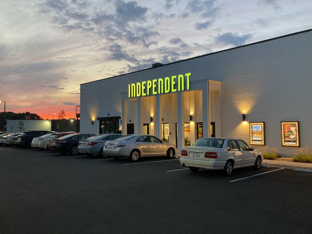 exterior of a building at sunset, the building has movie posters framed on the walls and big glowing letters above the entrance that read "Independent"