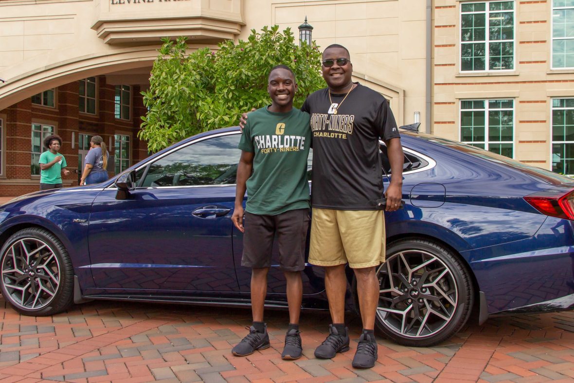 Charlotte student and parent standing in front of a blue car.