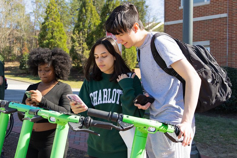 Two students looking at a phone next to Lime e-scooters.