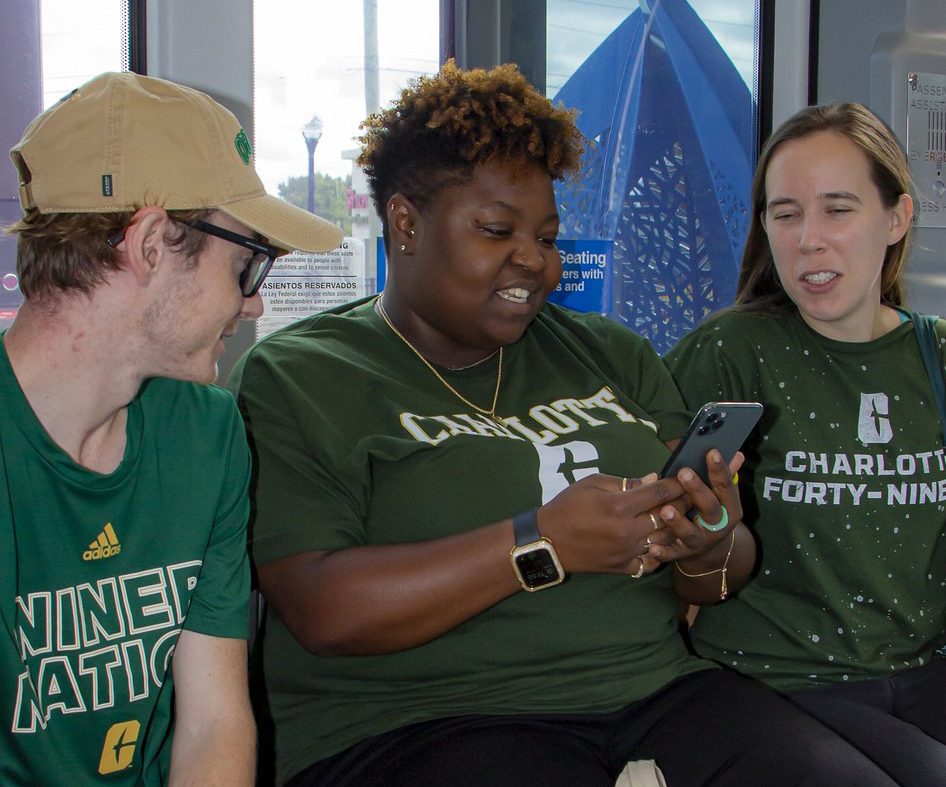 Three students on light rail bus looking at a phone.