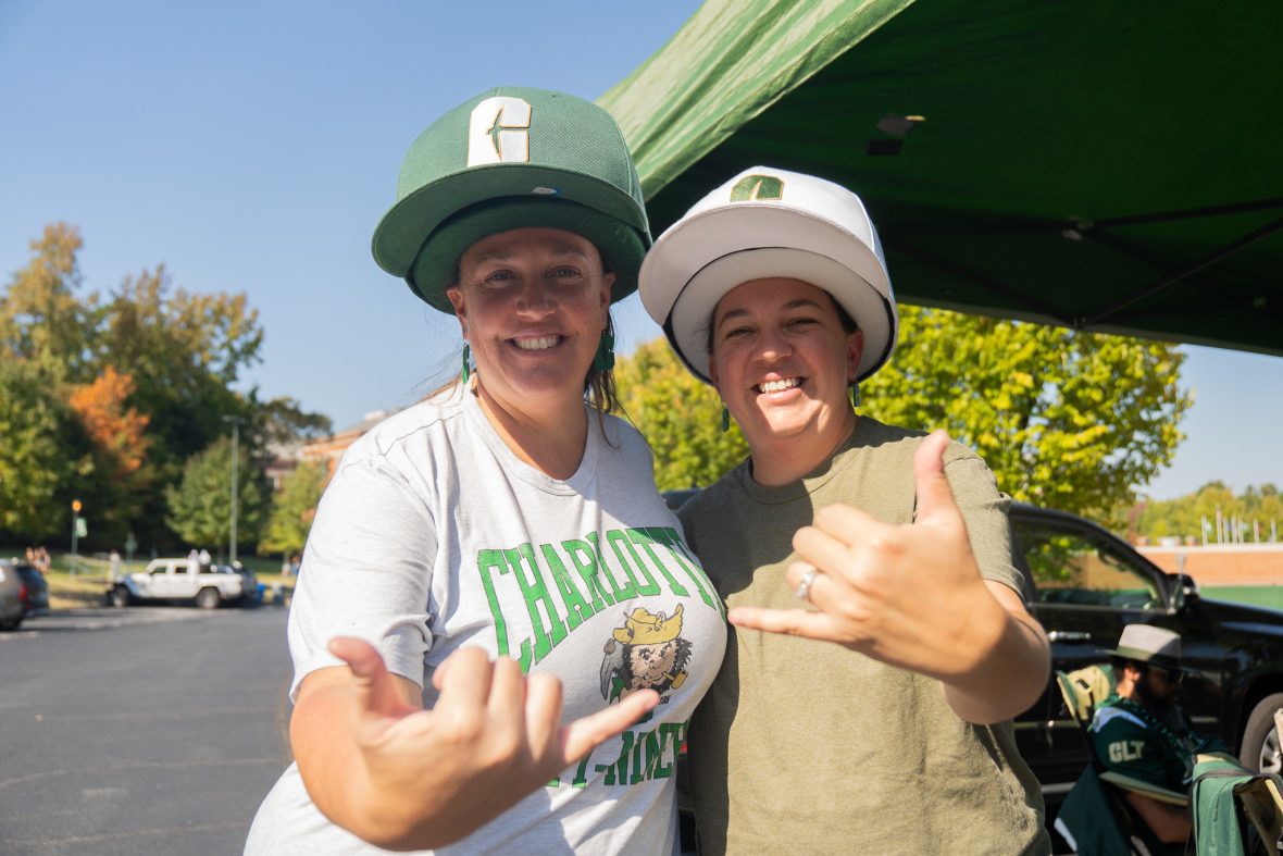 Two female fans smiling in large Niner hats with thumbs and pinkies extended