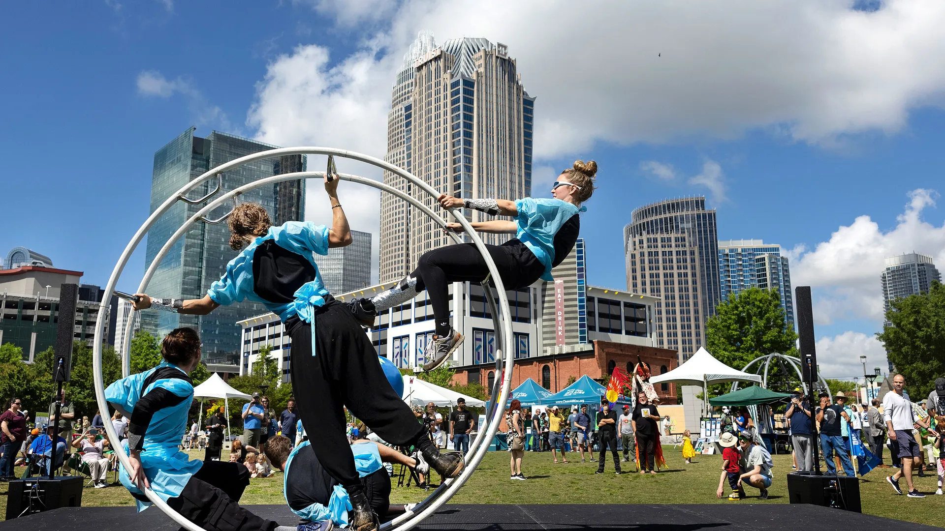 Aerial performers in hoops at an outdoor festival with the Charlotte skyline behind them.